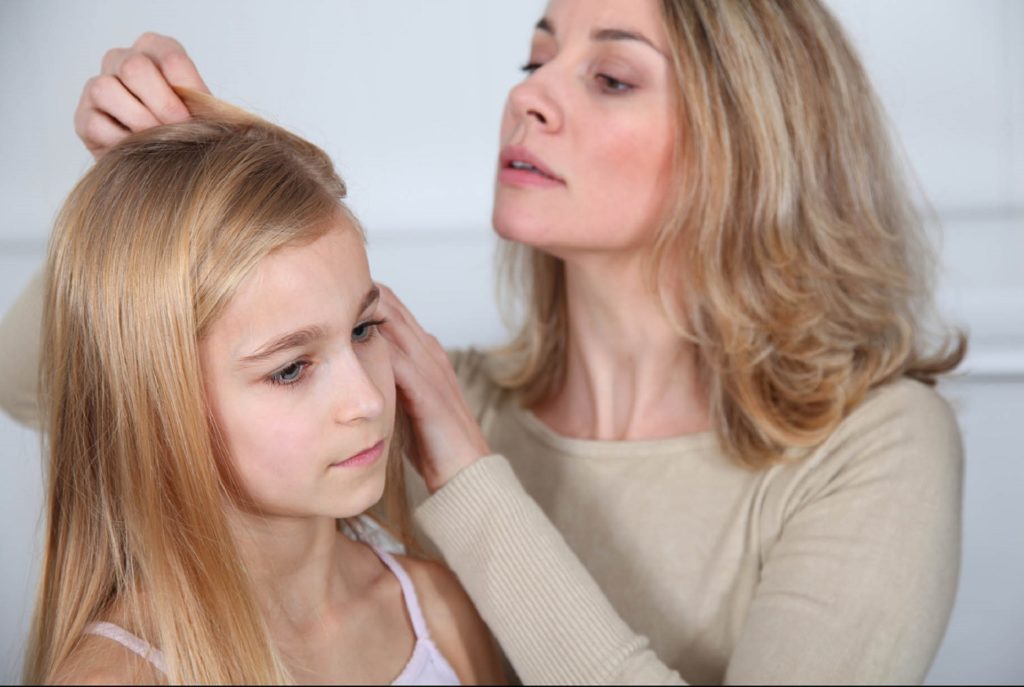 mamma che controlla se sua figlia ha i pidocchi nei capelli